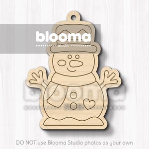 May include: Wooden snowman ornament with a hat, scarf, and heart detail. The snowman has a smiling face and outstretched arms. The ornament has a hole at the top for hanging. The text "blooma studio" is visible on the ornament.