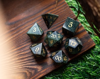 May include: A set of seven green and gold dice with various numbers on each face. The dice are on a wooden surface with green grass in the background.
