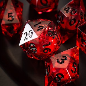 May include: A set of red, clear, and translucent dice with black numbers. The dice are a 20-sided die, a 12-sided die, a 10-sided die, a 4-sided die, a 6-sided die, and an 8-sided die.