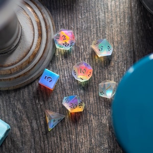 May include: A set of iridescent dice with black numbers on each face. The dice are on a wooden surface with a blue container and a white pedestal.