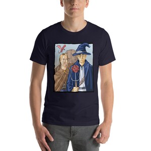 May include: A navy blue t-shirt with a graphic of a wizard and a woman standing in front of a castle. A red dragon flies above them. The wizard is holding a staff with a red twenty-sided die on top.