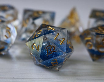 May include: A set of blue and gold dice with glitter embedded in the resin. The dice are numbered 1 through 12.