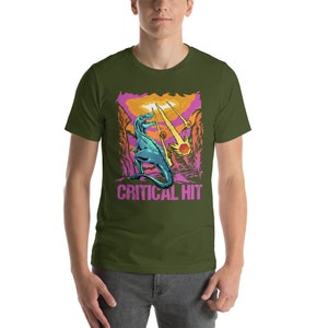 May include: A green t-shirt with a graphic of a blue dinosaur standing on a pink and orange landscape with the text "CRITICAL HIT" in pink.