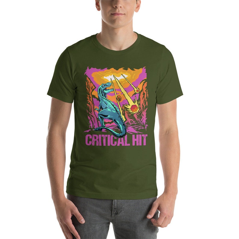 May include: A green t-shirt with a graphic of a blue dinosaur standing on a pink and orange landscape with the text "CRITICAL HIT" in pink.