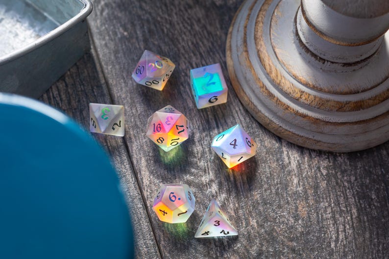 May include: A set of iridescent dice with rainbow colors and black numbers. The dice are on a wooden surface.