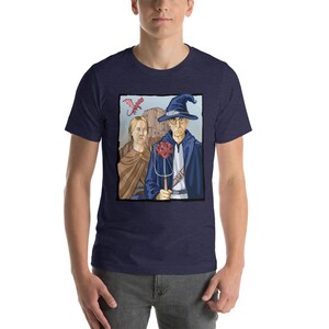 May include: A navy blue t-shirt with a graphic of a wizard and a woman standing in front of a castle. A red dragon flies above them. The wizard is holding a staff with a red dice on top.