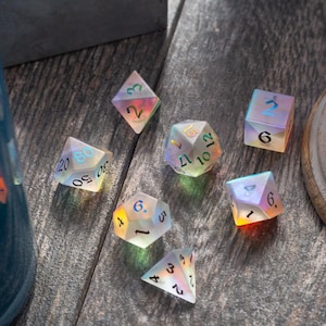 May include: Seven iridescent dice with black numbers on a wooden surface. The dice are in various shapes and sizes, including a d4, d6, d8, d10, d12, and d20.