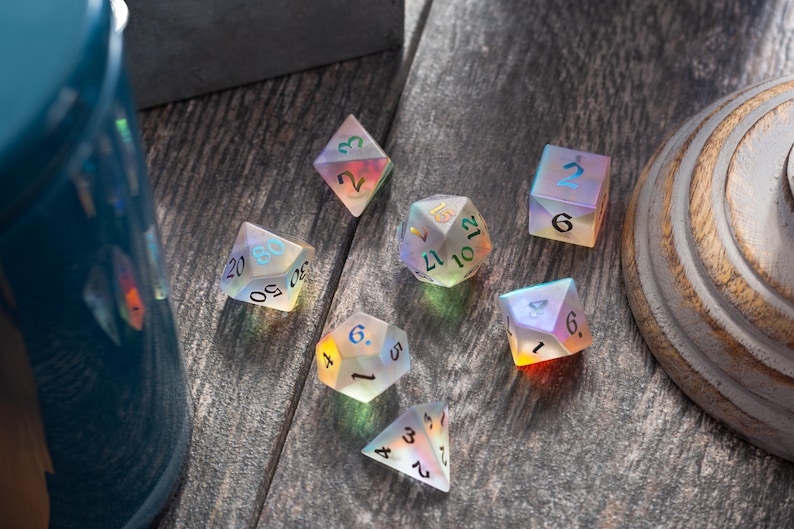 May include: Seven iridescent dice with black numbers on a wooden surface. The dice are in various shapes and sizes, including a d4, d6, d8, d10, d12, and d20.