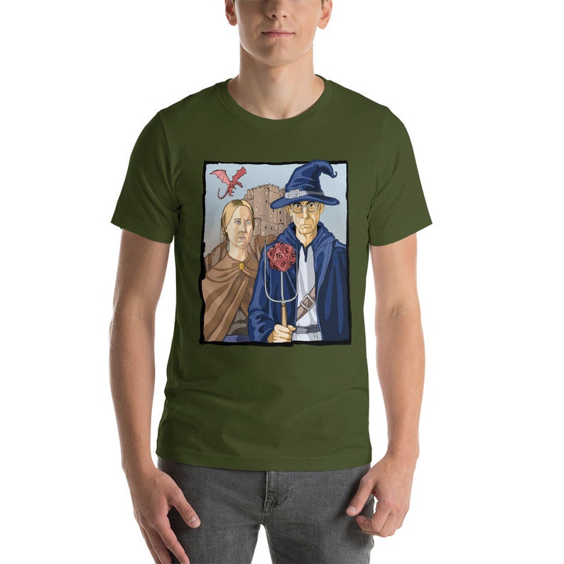 May include: A green t-shirt with a graphic of a wizard and a woman standing in front of a castle. The wizard is wearing a blue robe and a pointed hat. The woman is wearing a brown dress. A red dragon is flying in the sky above them.