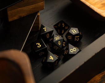 May include: A set of black and gold dice with numbers 2, 3, 4, 6, 7, 8, 10, 11, 12, 16, 20, and 00.