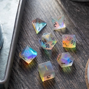 May include: A set of seven iridescent dice with black numbers. The dice are on a wooden surface.