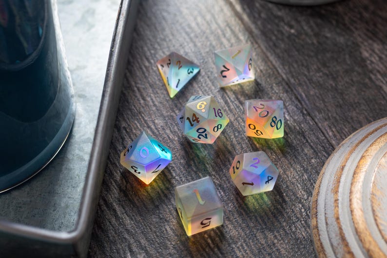 May include: A set of seven iridescent dice with black numbers. The dice are on a wooden surface.