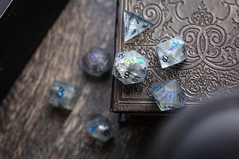 K&ouml;nnte beinhalten: Ein Satz irisierender W&uuml;rfel mit verschiedenen Zahlen auf jeder Seite. Die W&uuml;rfel liegen auf einer dunklen Oberfl&auml;che mit einem verzierten Design.