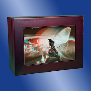 Puede incluir: Una caja de madera con una imagen 3D de un hada con alas sentada en una roca frente a un planeta con anillos. La imagen está en tonos de azul, rojo y blanco.