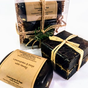 Puede incluir: Tres barras de jabón hecho a mano envueltas en papel marrón y cuerda. El jabón está etiquetado con "Lemongrass & Sage with Honey" y "Handmade with Natural Herbs and Essential Oils".