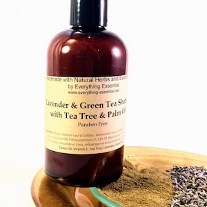 Puede incluir: Una botella marrón de champú de lavanda y té verde con árbol de té y aceite de palma. La botella está etiquetada con "Handmade with Natural Herbs and Essences by Everything Essential www.everything-essential.net". La botella está sobre un plato dorado con un platillo verde y un montón de lavanda seca.