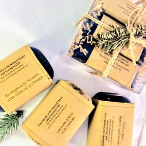 Puede incluir: Tres barras de jabón hecho a mano con hierbas naturales y aceites esenciales. Los jabones están envueltos en papel marrón con texto que dice "Hecho a mano con hierbas naturales y aceites esenciales" y enumera los ingredientes de cada jabón. Los jabones son de eucalipto y cúrcuma con carbón vegetal y avena, lavanda y rosa con avena, y hierba limón y salvia con miel.