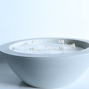 May include: A large, gray concrete bowl candle with multiple white wicks. The candle is unlit and the bowl has a textured surface.