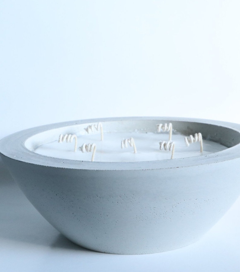May include: A large, gray concrete bowl candle with multiple white wicks. The candle is unlit and the bowl has a textured surface.