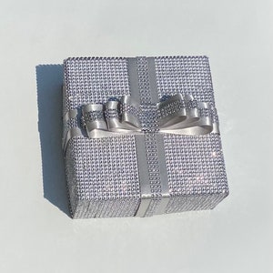 May include: A silver gift box with a sparkly, textured surface and a large silver bow. The box is tied with silver ribbon.