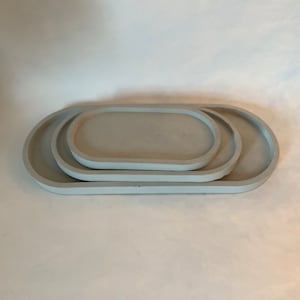 May include: Three gray oval-shaped concrete trays of different sizes stacked on top of each other.