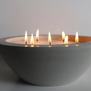May include: A gray concrete bowl candle with multiple wicks burning. The candle is lit and the flames are visible.