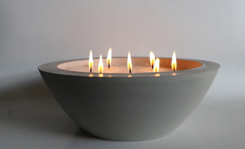 May include: A gray concrete bowl candle with multiple wicks burning. The candle is lit and the flames are visible.