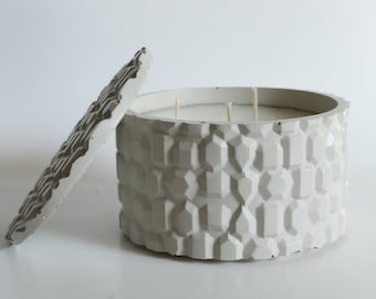 May include: A white concrete candle with a geometric pattern and a matching lid. The candle has three wicks and is in a cylindrical shape.