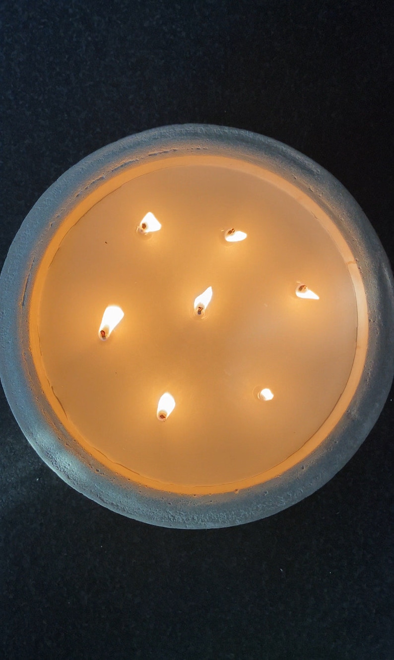 May include: A round, white candle holder with a textured surface. The candle holder has seven lit candles inside.