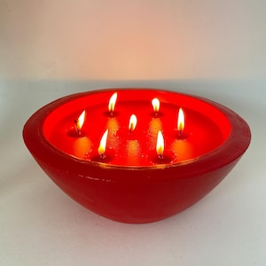May include: A red bowl-shaped candle with multiple wicks burning. The candle is lit and the flames are visible.