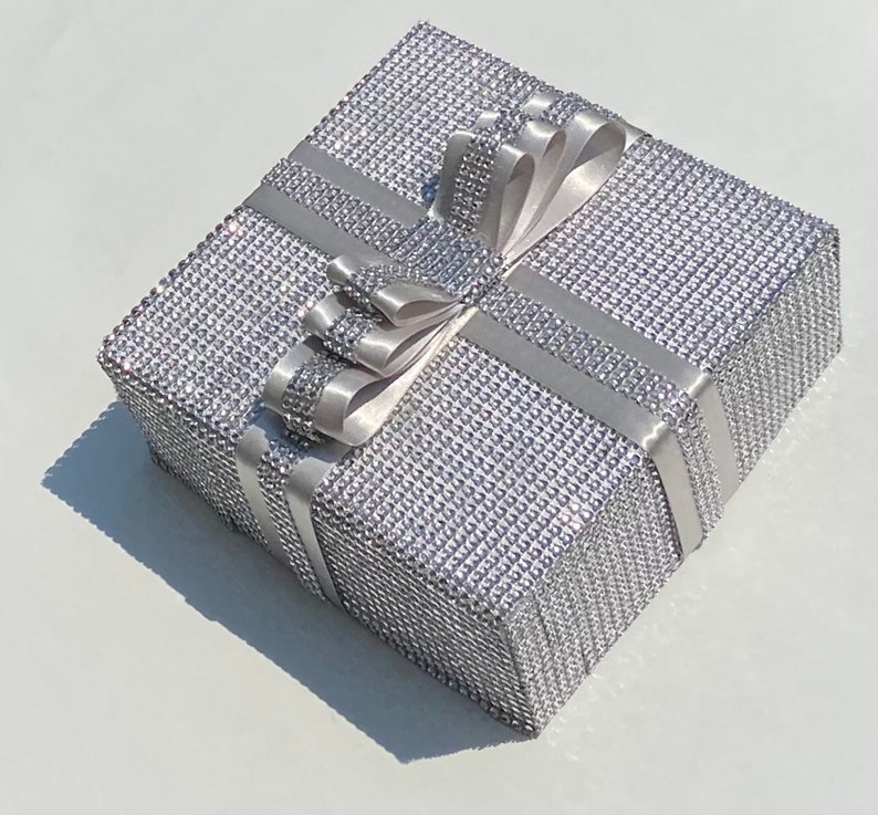 May include: A silver gift box with a sparkly, textured surface and a white satin ribbon tied in a bow.