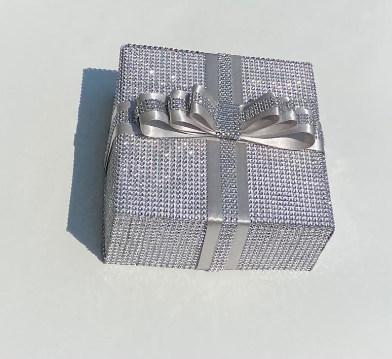 May include: A silver gift box with a sparkly, diamond-like finish. The box is tied with a silver satin ribbon and bow.