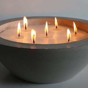 May include: A gray concrete bowl candle holder with seven lit candles. The bowl is round and has a smooth, textured surface.