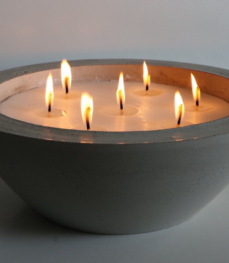 May include: A gray concrete bowl candle holder with seven lit candles. The bowl is round and has a smooth, textured surface.