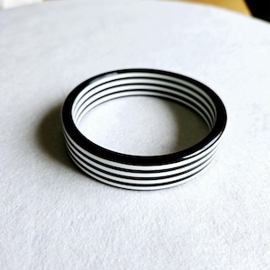Könnte beinhalten: Schwarz-weiß gestreiftes Armreif-Armband. Das Armband ist aus Kunststoff und hat eine glänzende Oberfläche.