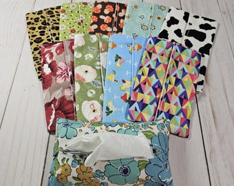 May include: A collection of colourful fabric tissue holders with various patterns, including floral, geometric, and animal prints. The holders are made of cotton fabric and have a white tissue box inside.
