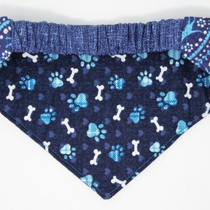 May include: A blue bandana with a white bone and paw print pattern. The bandana has a blue elastic band around the neck.