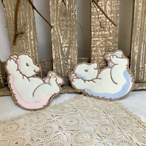 Peut inclure: Deux patchs en feutre brodés d'ours polaires, l'un en rose et l'autre en bleu, sur un fond en bois.