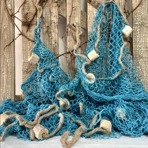 Peut inclure: Deux filets de pêche turquoise avec des cordes et des flotteurs en bois sont drapés sur un fond en bois avec des branches. Les filets sont d'un bleu vif et les flotteurs sont de couleur bois naturel. La corde est marron clair.
