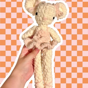 Puede incluir: Un peluche de ganchillo hecho a mano con forma de ratón bailarina. La figura está confeccionada con hilo color crema, con grandes orejas redondas con lazos rosa claro, un tutú rosa suave y detalles de cinta rosa envueltos en la parte inferior.