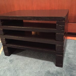 May include: A black wooden stacking shelf unit with four tiers. The shelf unit is made of solid wood and has a simple, modern design.