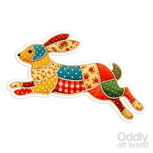 May include: A colorful patchwork rabbit sticker in a leaping pose. The design features various fabric patterns, including polka dots, floral prints, and gingham. The rabbit's ears and feet are red with floral accents, and the body is a mix of yellow, blue, red, and green patches.