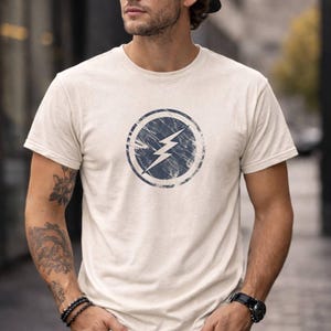 Distressed lightning bolt graphic t-shirt with circular emblem printed on ringer and classic cotton tees in multiple color options