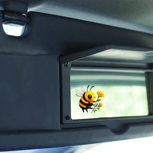 Adorable die-cut vinyl design of a fuzzy yellow honeybee holding a bright yellow flower. Shown as a fridge magnet displayed on a stainless steel refrigerator. This design is also available as a waterproof transparent sticker in five sizes. Ideal for decorating laptops, journals, water bottles, fridges, and more. Suitable for indoor and outdoor use.