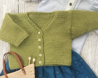 May include: A green knitted cardigan with a v-neck and button closure. The cardigan is laying on a blue and white patterned fabric.