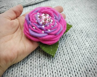 May include: A pink and purple felt flower brooch with a green felt leaf. The flower has a centre of white and pink beads.
