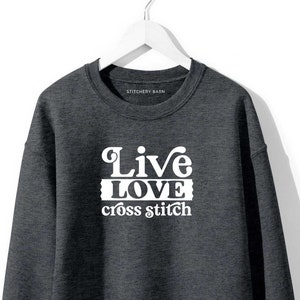May include: A dark grey sweatshirt with the text "Live Love cross stitch" in white.
