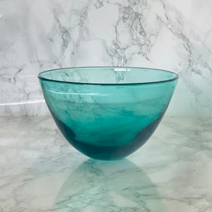 May include: A teal glass bowl with a rounded shape. The bowl is sitting on a white marble surface.