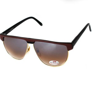 May include: Brown and black sunglasses with gold accents and brown lenses. The sunglasses have a UV eye protection label.