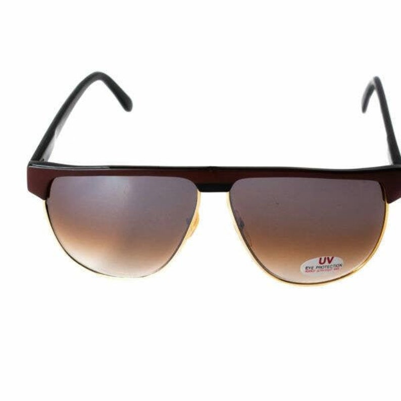 May include: Brown and black aviator sunglasses with gold trim and brown gradient lenses. The sunglasses have a "UV Eye Protection" label on the right lens.